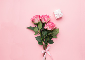 A bouquet of fresh roses and a gift on a pink background. Flat layout. Copy space. Minimalism.