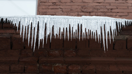 Roof of old building covered with sharp icicles, copy space, horizontal/ Ice stalactite hanging from the roof/ Poor thermal insulation of the roof leads to the formation of icicles