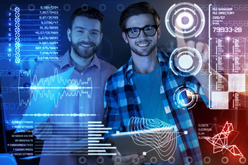 New program in use. Cheerful professional IT men touching a transparent screen while being involved in work