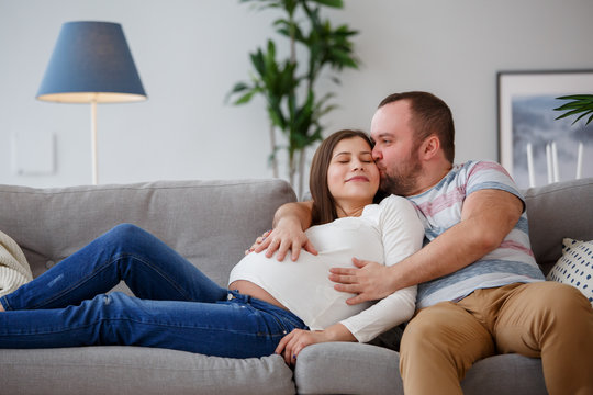 Photo of hugging pregnant woman and man on gray sofa