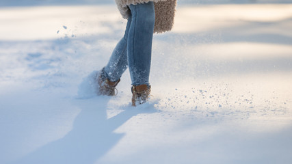 Woman's feet in winter boots walking in snow or snowdrifts at sunny frosty day, close up, copy...