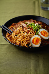 Japanese ramen with pork belly, mushrooms and marinated eggs on green linen tablecloth