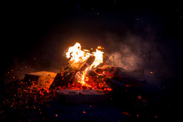 Burning wood at night. Campfire at touristic camp at nature in mountains. Flame amd fire sparks on dark abstract background. Cooking barbecue outdoor. Hellish fire element. Fuel, power and energy.