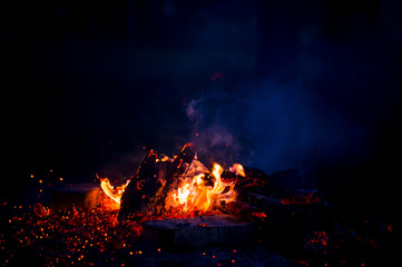Fototapeta na wymiar Burning wood at night. Campfire at touristic camp at nature in mountains. Flame amd fire sparks on dark abstract background. Cooking barbecue outdoor. Hellish fire element. Fuel, power and energy.