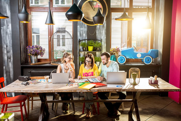 Group of caucasian coworkers dressed casually working together with documents and laptops at the big table in the beautiful cafe interior