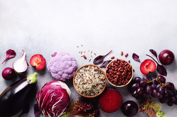 Purple vegetables, fruits on grey background. Violet eggplant, beets, cauliflower, purple beans, plums, onion, cabbage, grape, quinoa, rice. Ingredients for cooking, copy space, top view, flat lay