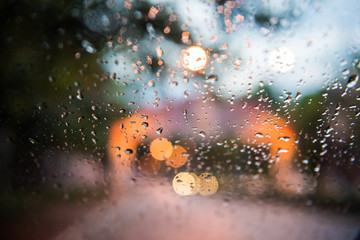 Rain drops on window with road light bokeh, City life in night in rainy season abstract background