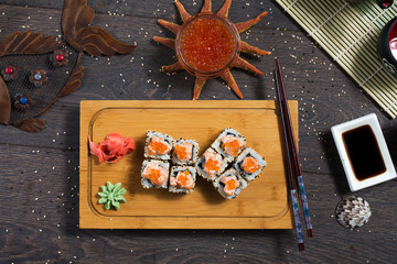 Sushi rolls served on a wooden plate in a restaurant. Sushi rolls and caviar on black wooden table. Japanese food.