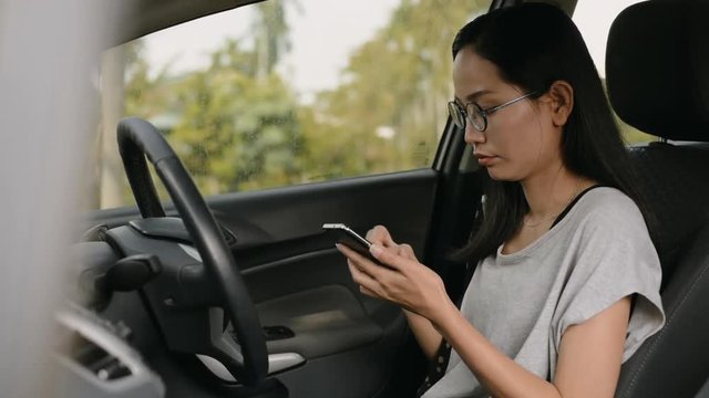 
Asian woman sits in the car and works on smartphone.