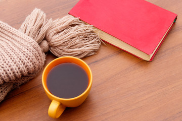 Cup of coffee, knitted scarf and book on wooden background