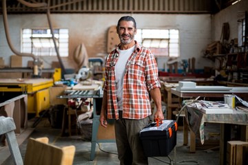 Portrait of carpenter standing with tool box