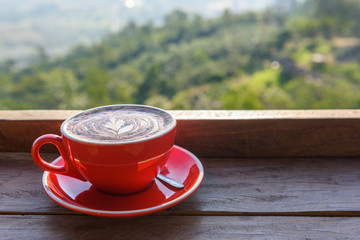 coffee in a red cup on a wooden table  in front of hill