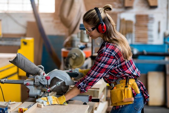 Female carpenter cutting wooden plank with electric saw 