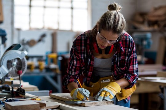 Female carpenter marking on wooden plank with pencil