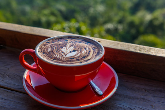 coffee in a red cup on a wooden table  in front of hill