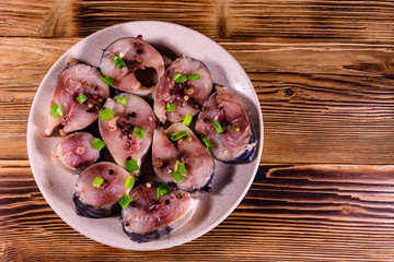 Sliced scomber fish with green onion on a ceramic plate on wooden table. Top view