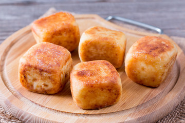 Cottage cheese pancakes in the form of cubes on a chopping wooden board