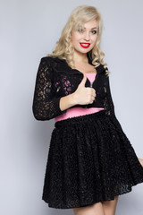 Portrait of a beautiful young blonde woman in a black lace suit. Girl posing in studio on gray background