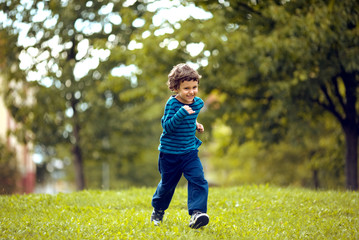 Cute boy running across grass und smiling.