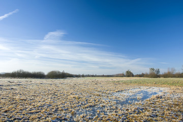 Frost on a wet meadow and white clouds