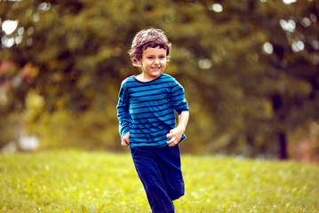 Cute boy running across grass und smiling.