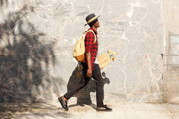 side portrait of young african american man walking outside with skateboard