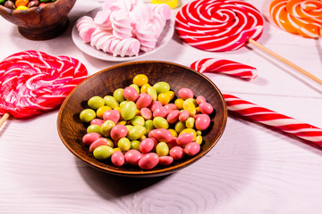 Ceramic plate with colored candies, candy cane, lollipops and marshmallows on a wooden table