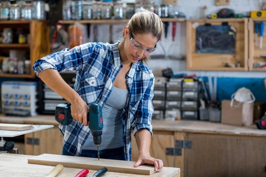 Female carpenter drilling a hole in a wooden plank