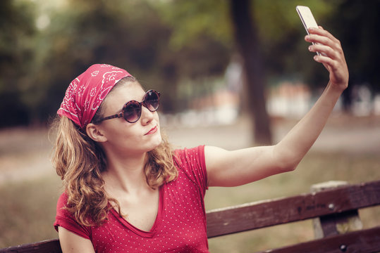 Young woman in a red retro dress taking a selfie, posing in front of her cell phone camera