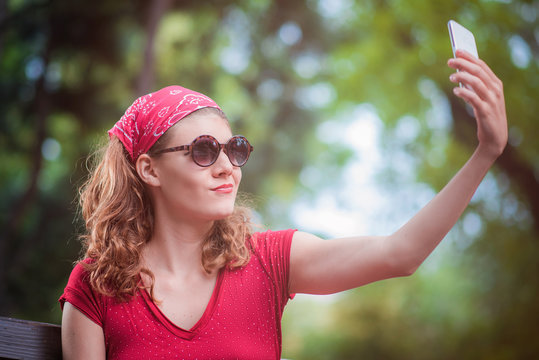 Young woman in a red retro dress taking a selfie, posing in front of her cell phone camera