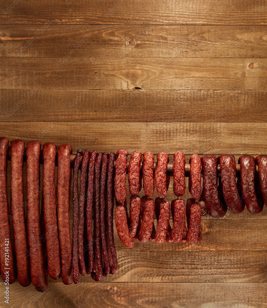 Wall mural Composition of different type of sausage hanged on wooden background