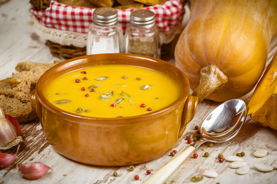 Homemade pumpkin soup in a clay bowl on rustic white table