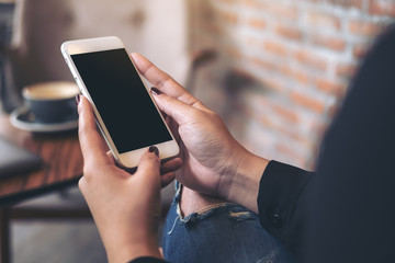 Mockup image of woman's hands holding and using white mobile phone with blank black desktop screen in cafe