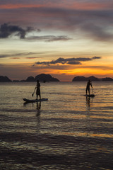 Fototapeta premium two man silhouette standing on sup boards on sunset time in El Nido, Palawan, Philippines, Corong Corong beach