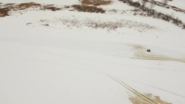 ATV race on the snow. Aerial view: Rider driving in the quadbike race. Man riding ATV in sand in protective clothing and a helmet. Racer rides a quad motorbike in the cross racing. Quadrocycle on the