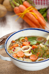 Vegetable soup in a metal bowl on a rural rustic wooden table.