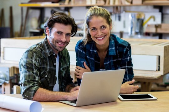 Portrait of male and female carpenters using a laptop in workshop