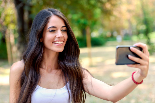 Young Beauty with long brown hair looking at smartphone taking photo of herself