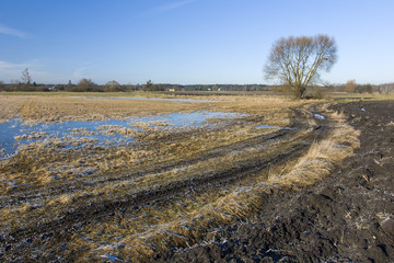 Long muddy country road through meadows and fields
