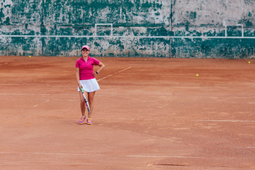 Tennis player. Cheerful beautiful woman in sportswear, standing on the court with tennis racket, looking at camera. Sport concept.