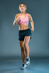 Fototapeta na wymiar Young beautiful woman in fitness wear runs over blue grey background. The athlete runs to the camera and looks up. An inspired girl runs to meet her dream