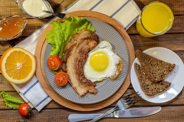 English Breakfast: fried egg with bacon, orange juice, tomatoes, zernovoi bread, lettuce leaf, top view.