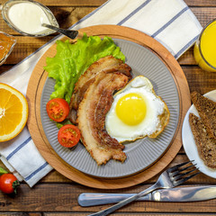English Breakfast: fried egg with bacon, orange juice, tomatoes, zernovoi bread, lettuce leaf, top view.