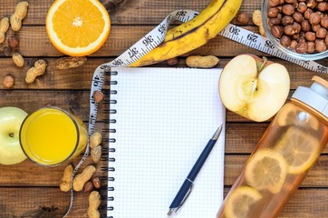 Healthy lifestyle; fitness bottle; fruits (oranges; apples and bananas); hazelnuts and peanuts; orange juice, a pen and a notebook and measuring tape. Top view; the concept of free space for text