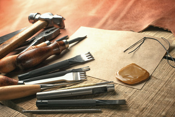 Set of leather craft tools on wooden background. Workplace for shoemaker. Piece of hide and working handmade tools on a work table.