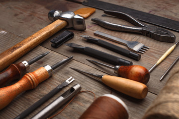 Set of leather craft tools on wooden background. Workplace for shoemaker. Piece of hide and working...