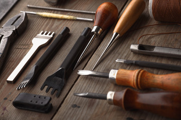 Set of leather craft tools on wooden background. Workplace for shoemaker. Piece of hide and working...