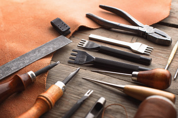 Set of leather craft tools on wooden background. Workplace for shoemaker. Piece of hide and working handmade tools on a work table.