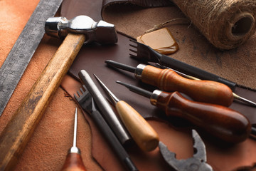 Set of leather craft tools on wooden background. Workplace for shoemaker. Piece of hide and working handmade tools on a work table.