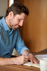 Young man writing in a notebook while working from home